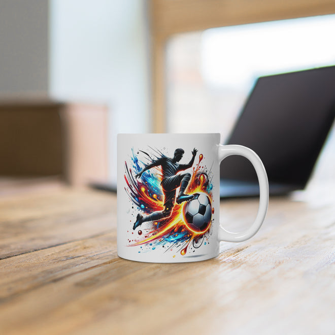 Weiße Kaffeetasse mit einem dynamischen Fußball-Design, das einen Spieler zeigt, der vor einem weissen Hintergrund einen Fußball tritt, positioniert auf einem Schreibtisch.